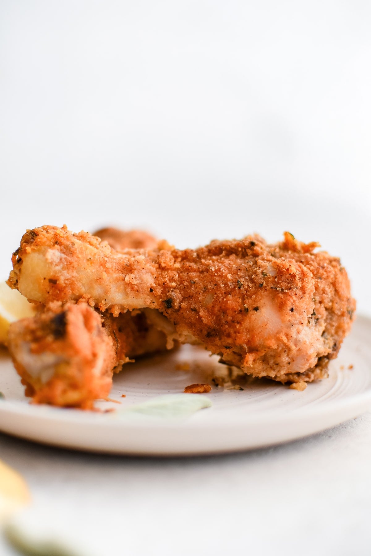 Two homemade shake and bake chicken drumsticks on a white plate.