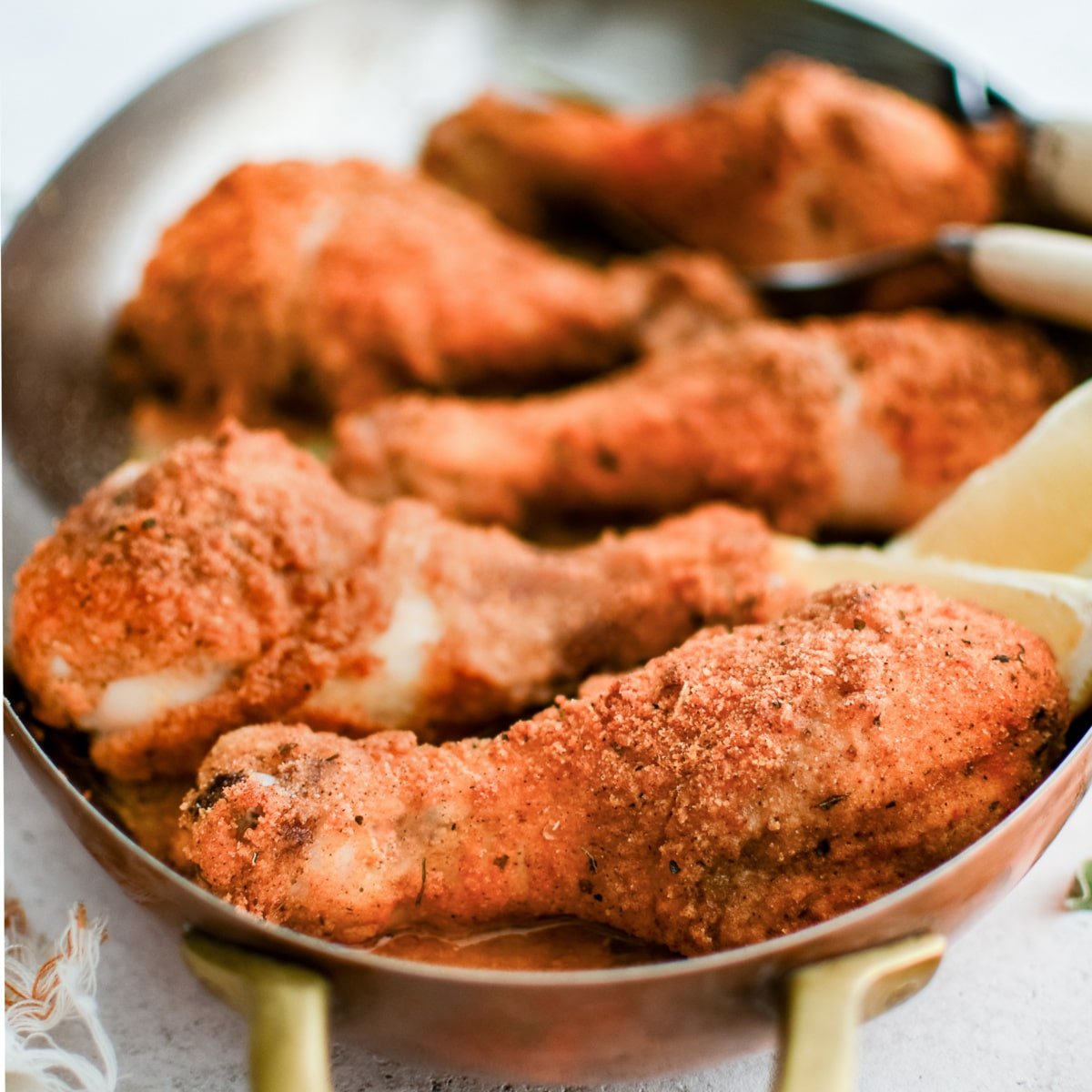 Oval-shaped baking dish filled with five golden, crispy baked chicken drumsticks coated in shake and bake seasoning.