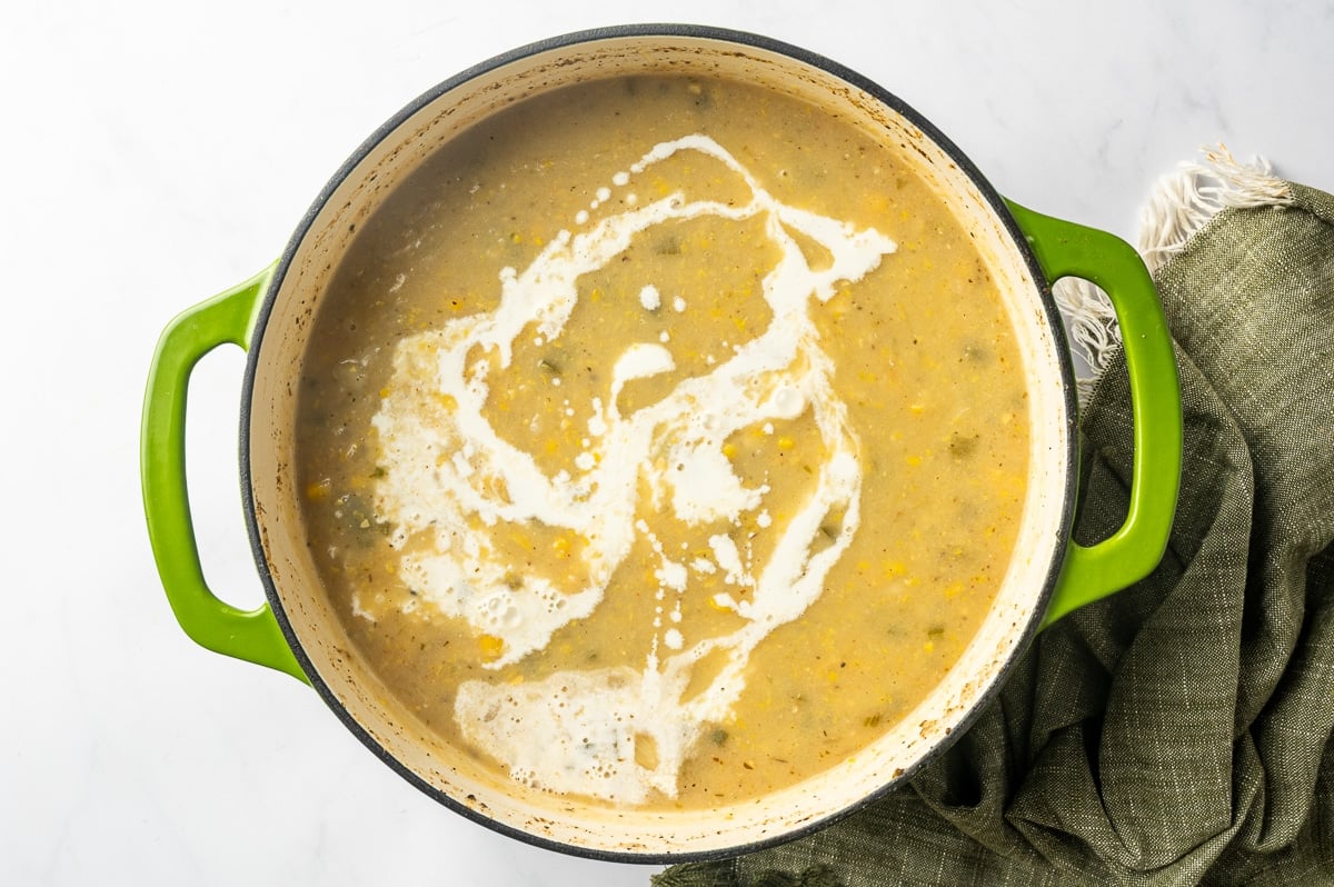 Heavy cream swirled across the surface of partially blended chicken corn chowder before being stirred into the thickened soup.