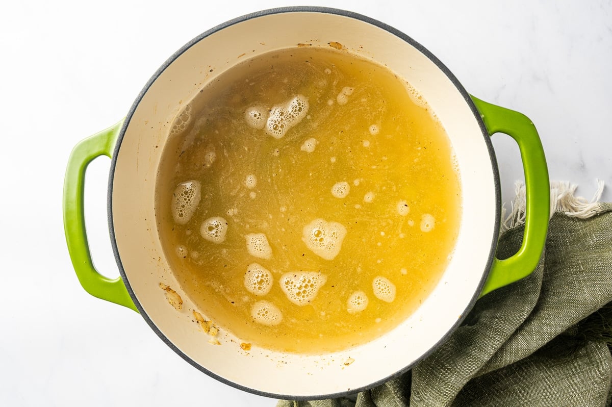 Golden chicken broth in a Dutch oven with cooked vegetables and seasonings visible throughout the liquid, forming the base of the chicken corn chowder.
