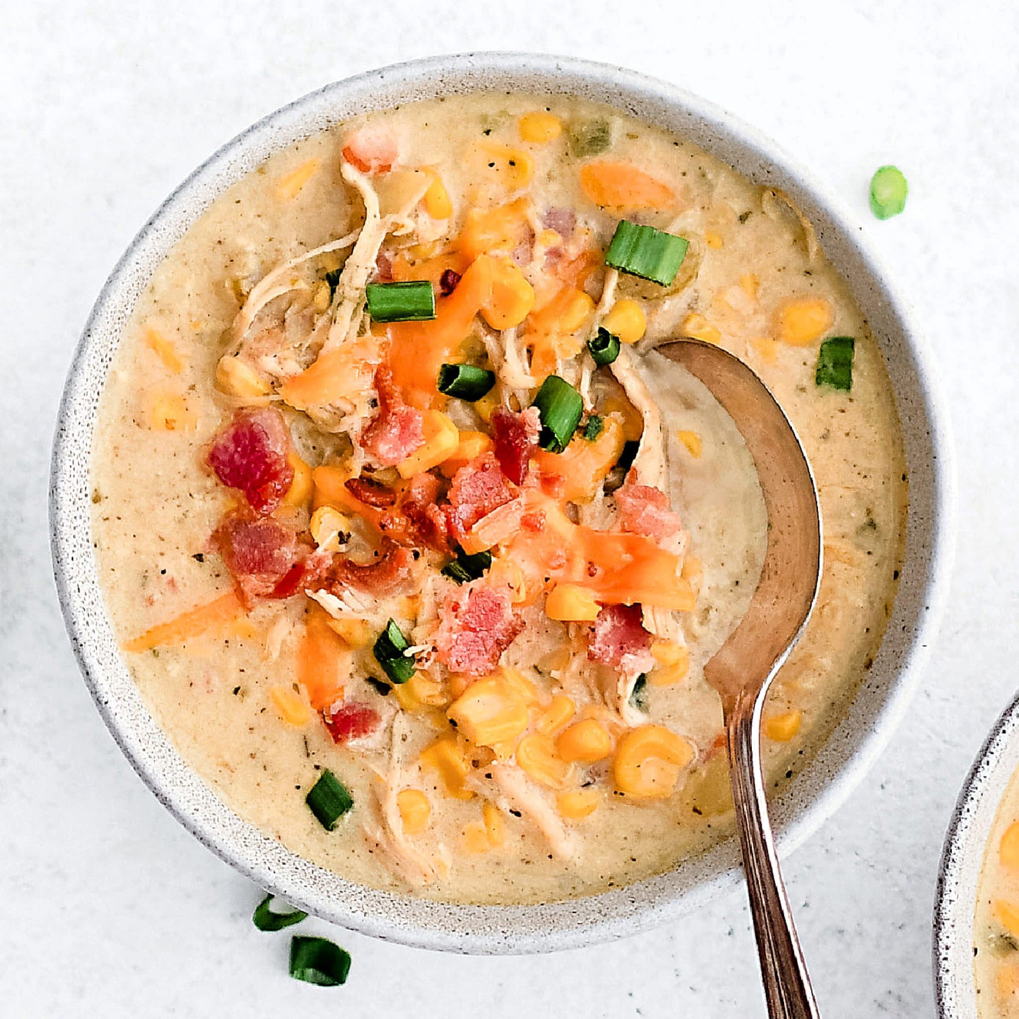 White soup bowls filled with corn and chicken chowder and garnished with shredded cheddar cheese, crispy bacon, and green onions.