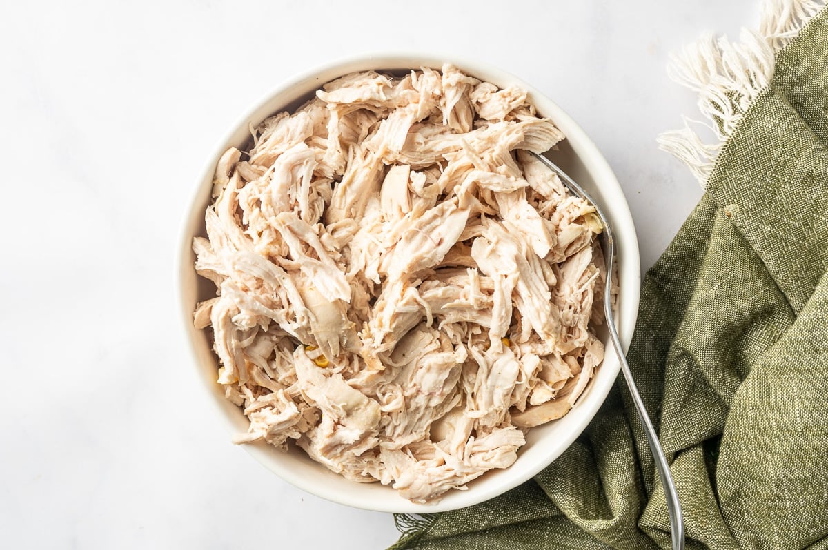 Cooked chicken breast shredded into bite-size pieces in a white bowl with a spoon, ready to be returned to the chicken corn chowder.