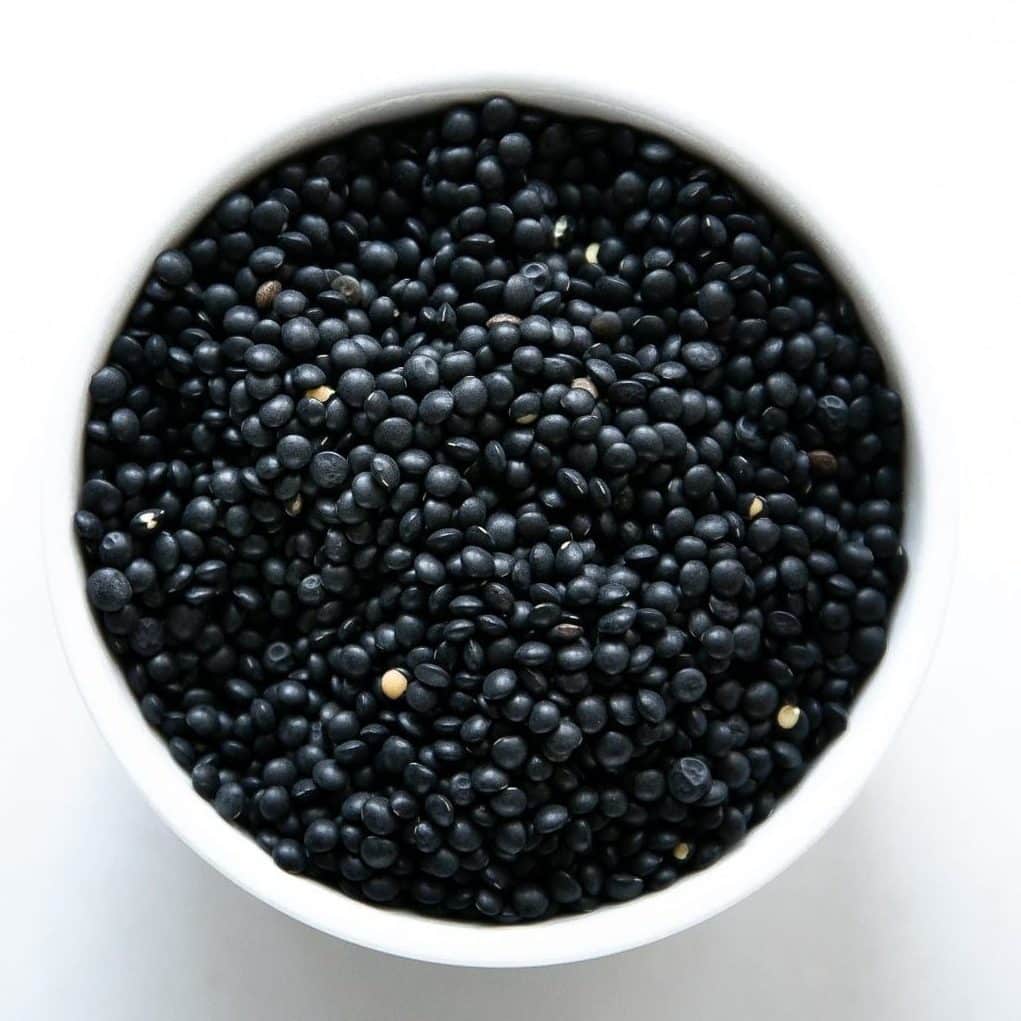 White bowl filled with dried black (Beluga) lentils.
