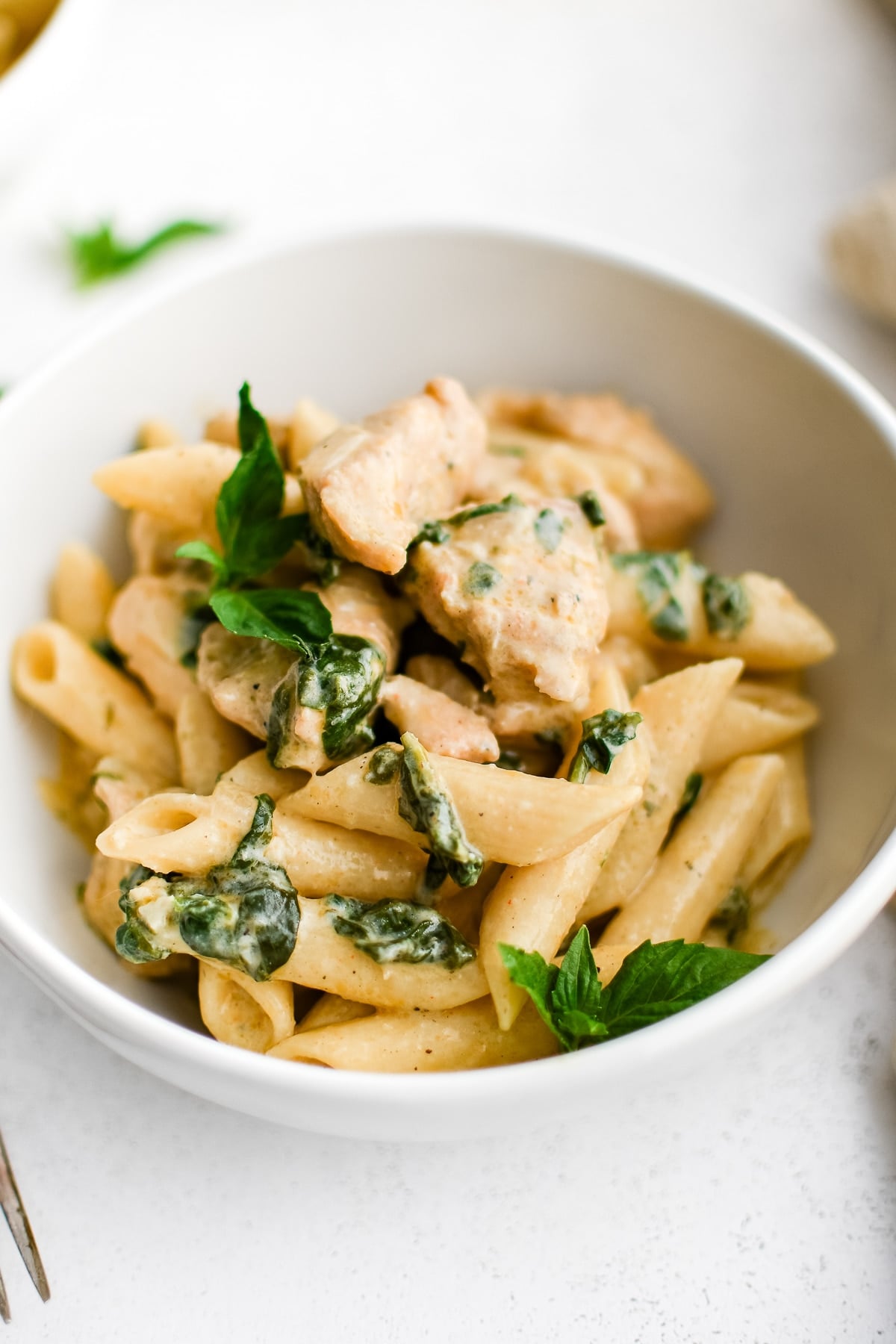 White bowl filled with penne pasta in a creamy Boursin cheese sauce with cooked cubes of chicken and spinach.
