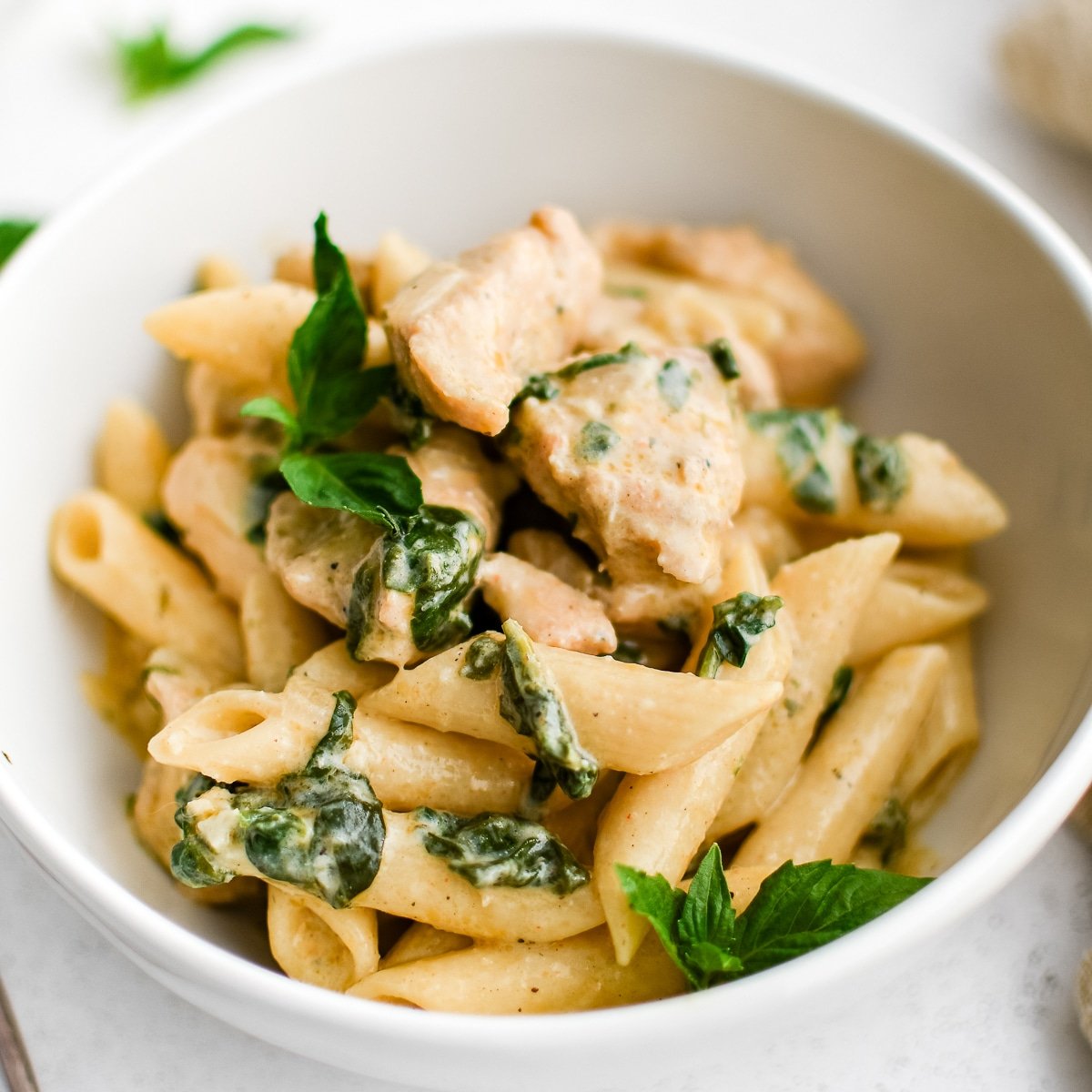 White bowl filled with penne pasta in a creamy Boursin cheese sauce with cooked cubes of chicken and spinach.