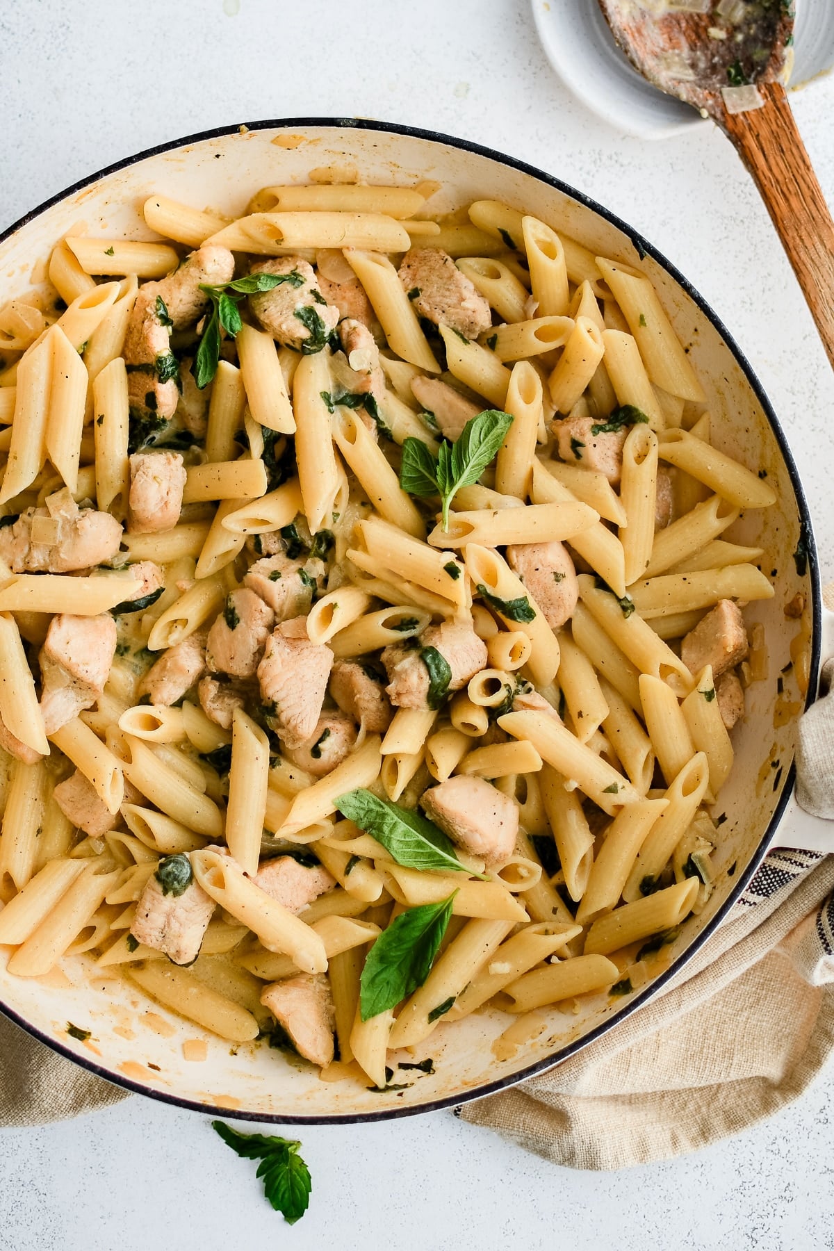 Large ceramic pan filled with penne pasta in a creamy Boursin cheese sauce with cooked cubes of chicken and spinach.