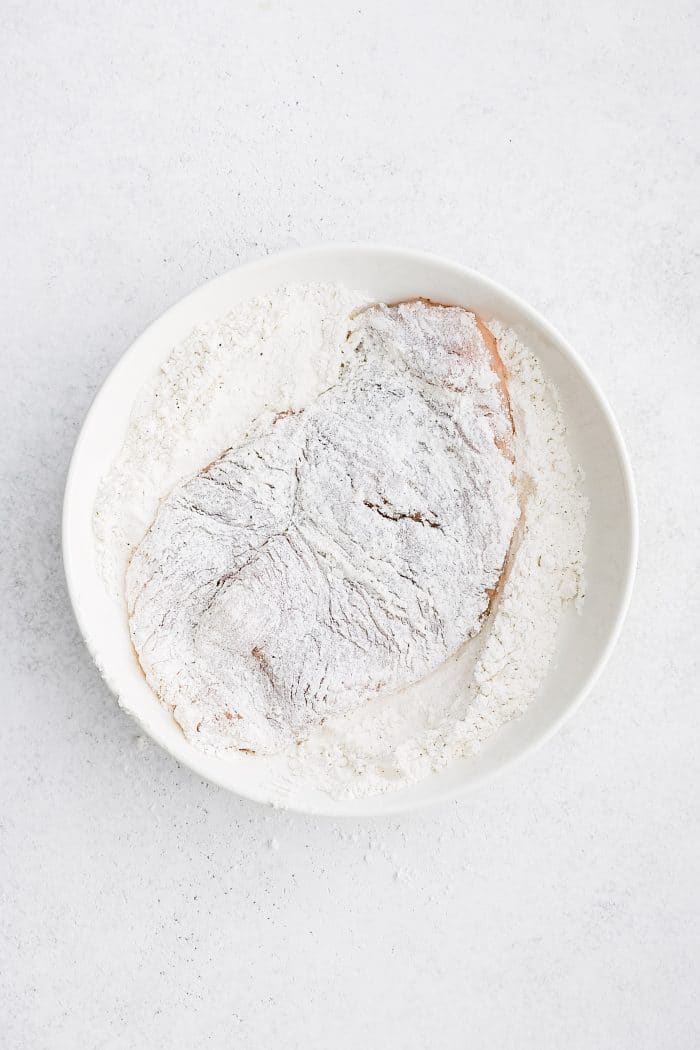 Shallow bowl filled with chicken cutlet coated in flour.