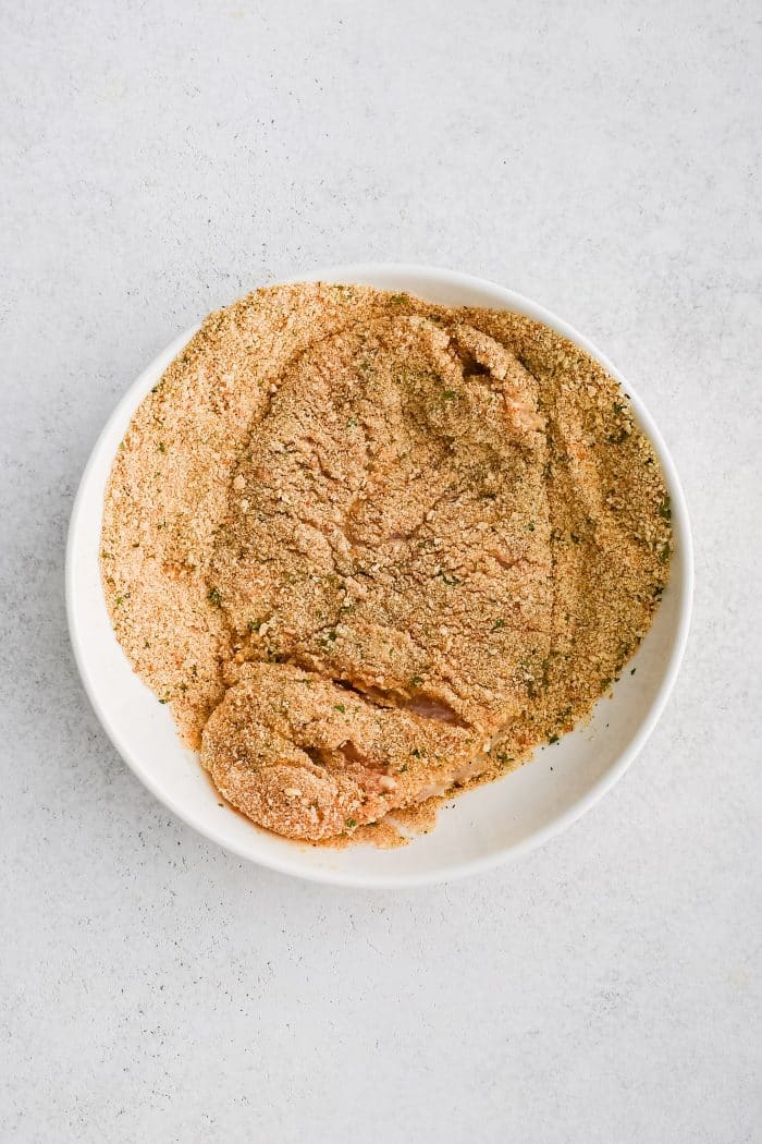 Coating a chicken cutlet in breadcrumb and parmesan coating.