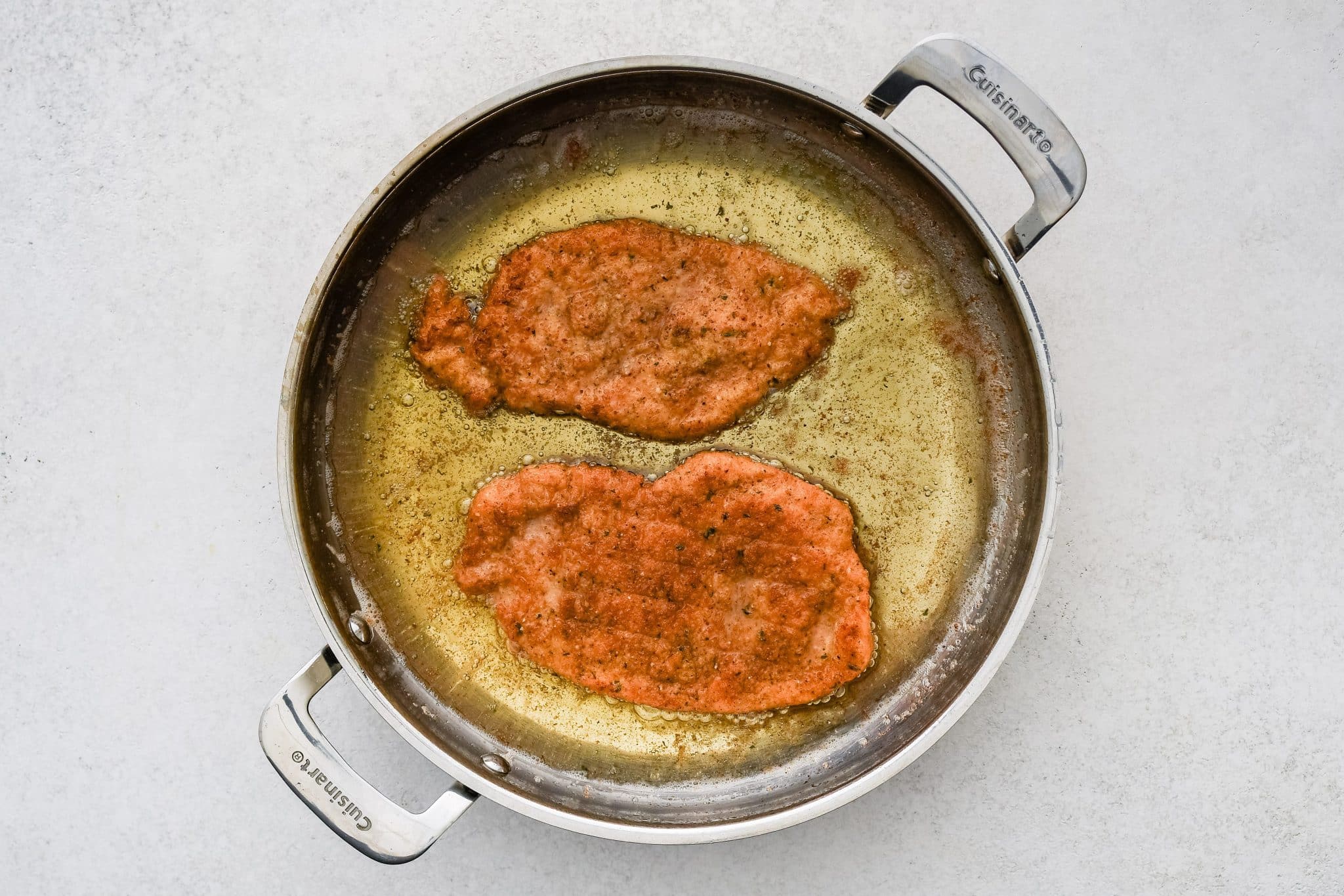 Two thinly sliced chicken cutlets breaded and frying in oil.