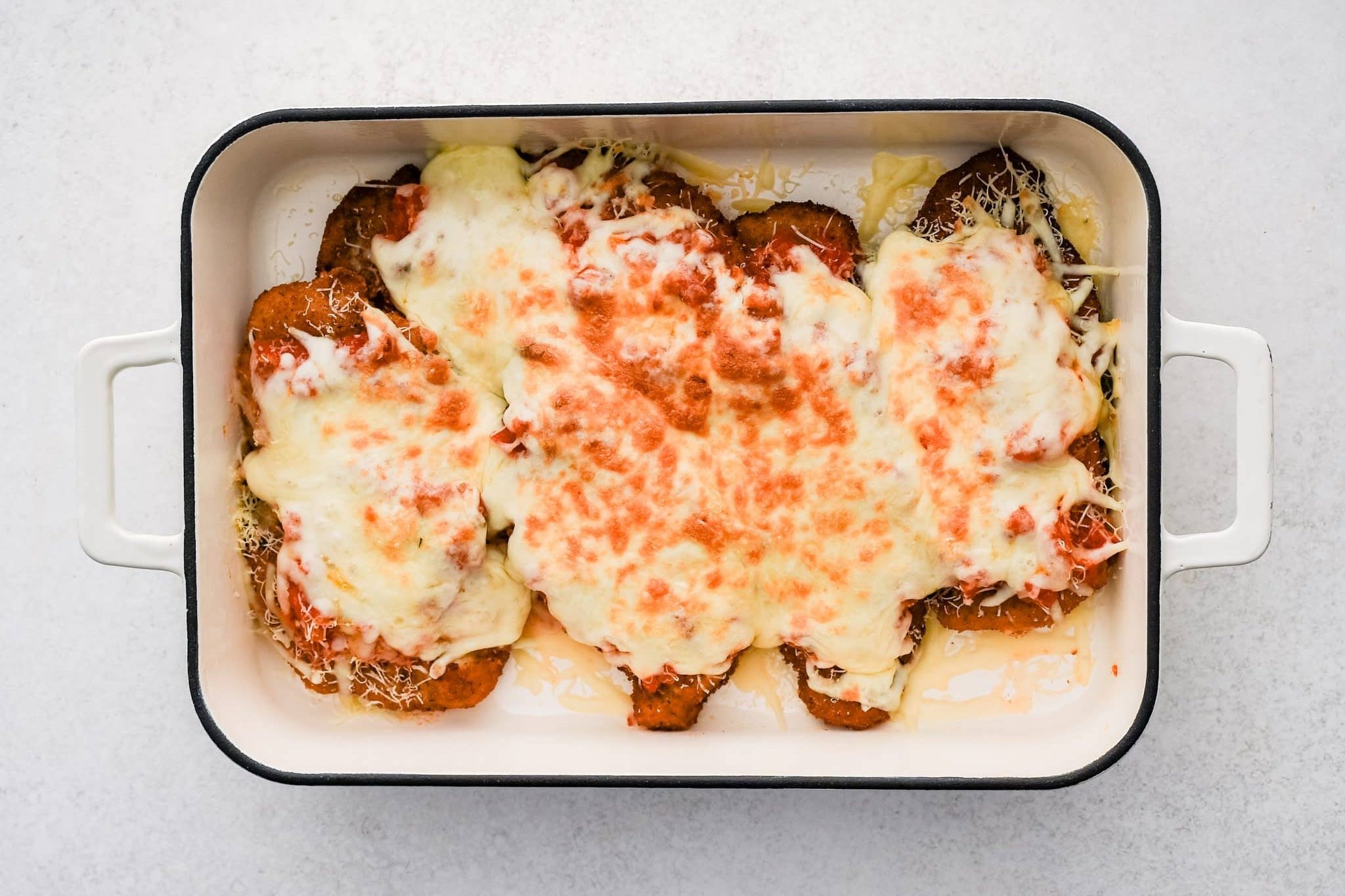 Large baking dish with breaded fried chicken cutlets topped with homemade tomato sauce and melted cheese.