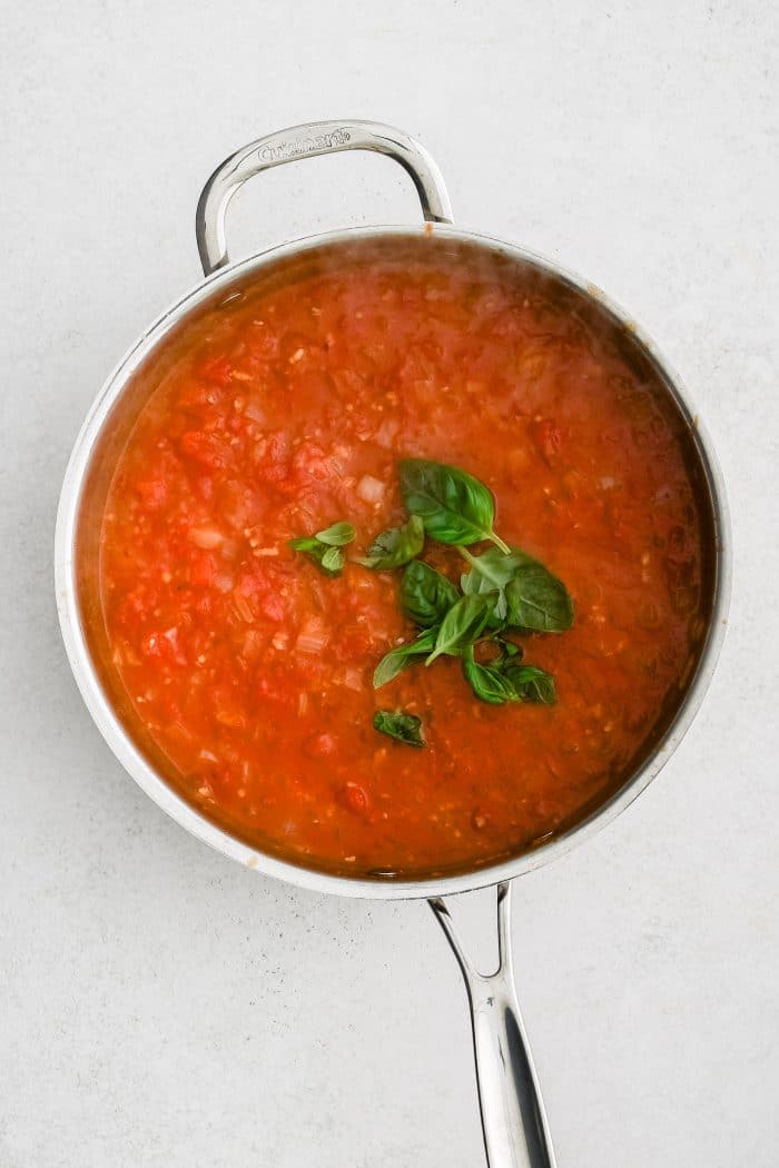 Fresh basil added to a pot filled with homemade marinara sauce.