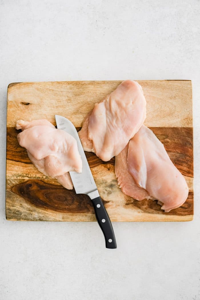 Chefs knife slicing whole chicken breasts in half horizantally.