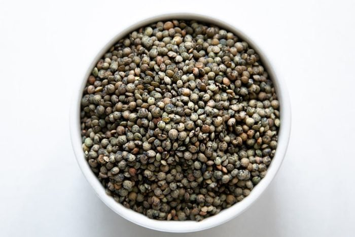 White bowl filled with dried French (Puy) lentils.