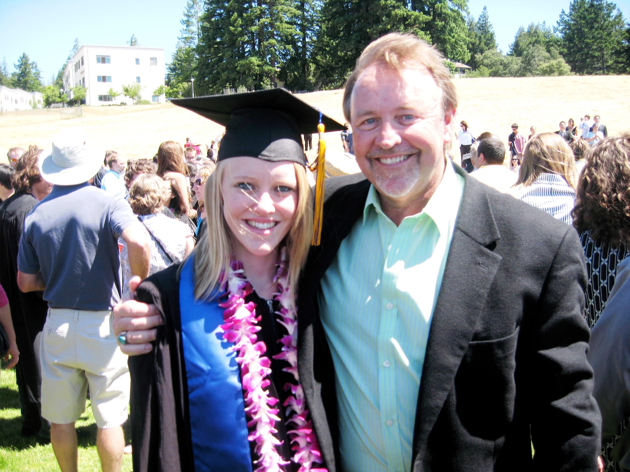 Jessica Randhawa wearing a graduation cap, gown, blue stole, and flower lei while standing with her father at the University of California, Santa Cruz graduation ceremony.
