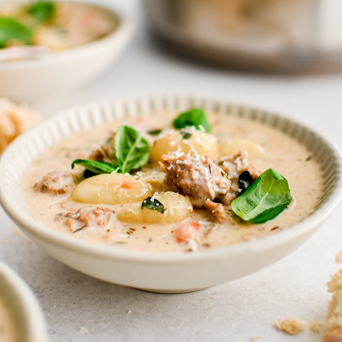 White soup bowl filled with creamy Italian sausage and gnocchi soup garnished with grated parmesan cheese and fresh basil leaves.