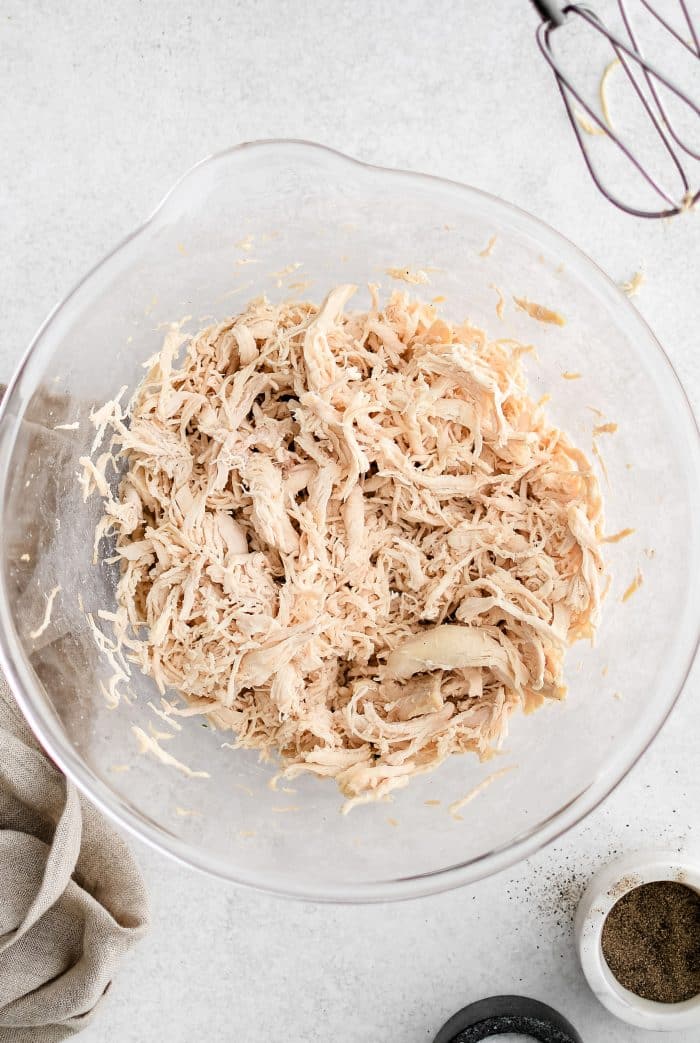 Shredded cooked chicken breast in a large glass bowl.