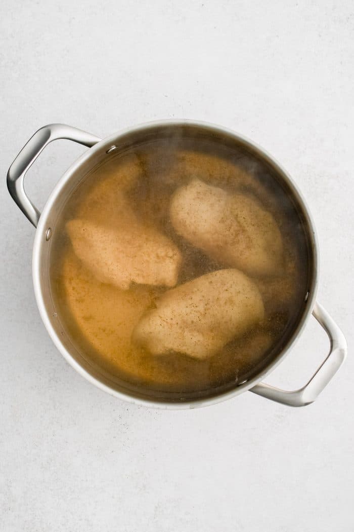 Three chicken breasts in a pot filled with boiled water seasoned with salt and water.