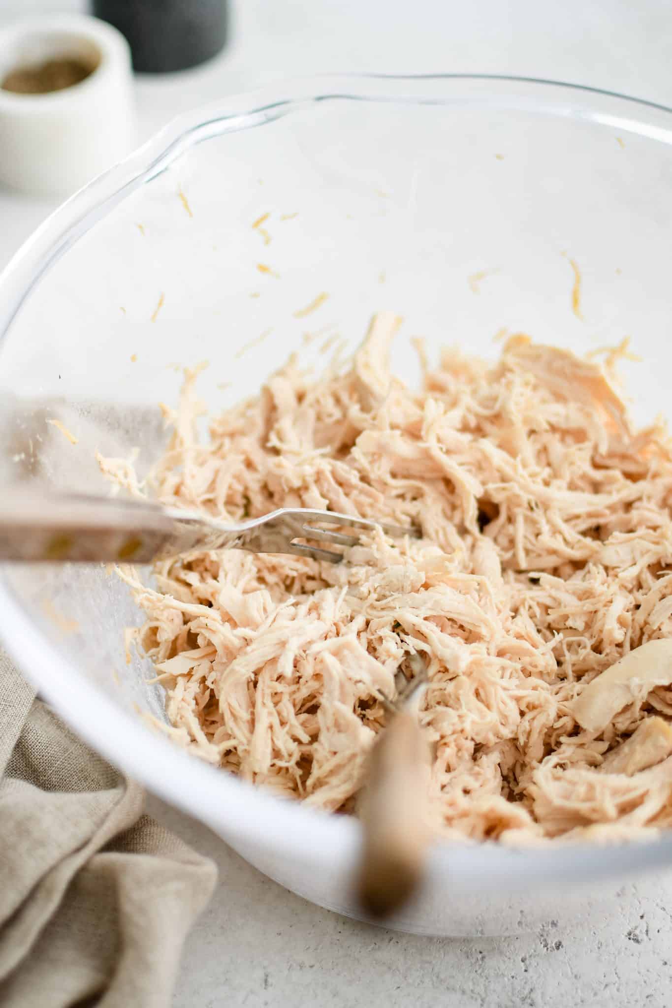 Shredded cooked chicken breast in a large glass bowl with two forks.