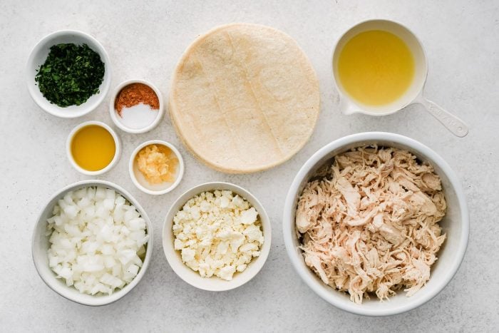 All of the ingredients needed to make Shredded Chicken Tacos in individual bowls, measuring cups, and ramekins.