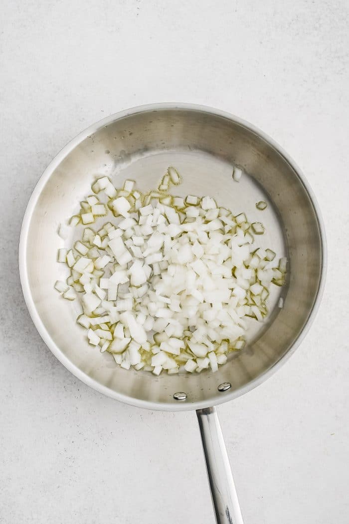 Large stainless steel skillet with olive oil and diced onion.