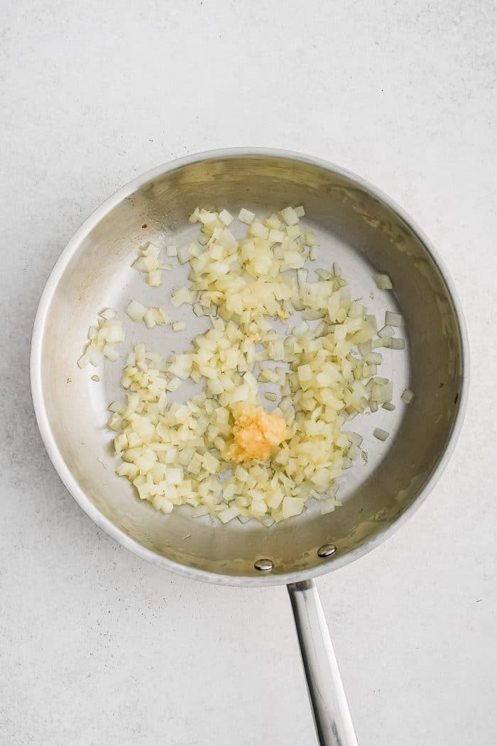 Large stainless steel skillet with softened diced onion and minced garlic.