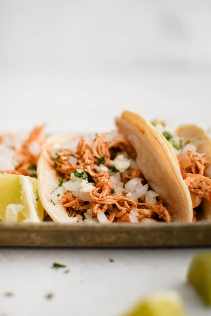 Shredded chicken taco topped with minced white onion and cilantro and served with fresh lime wedges.