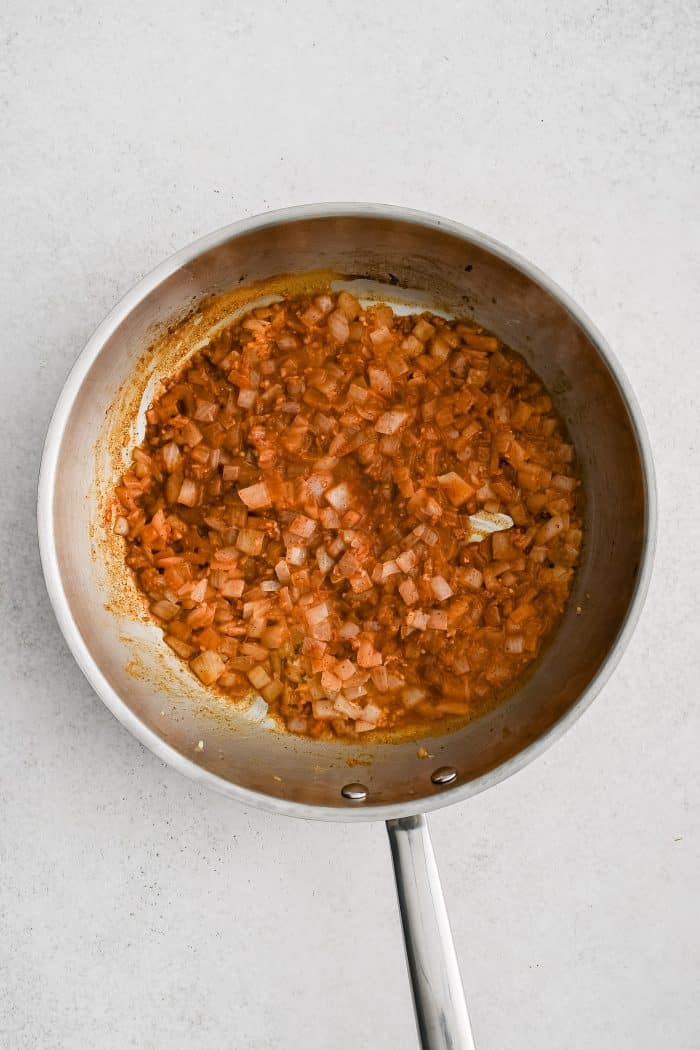 Large skillet filled with onion, taco seasoning, garlic, and chicken broth simmering.