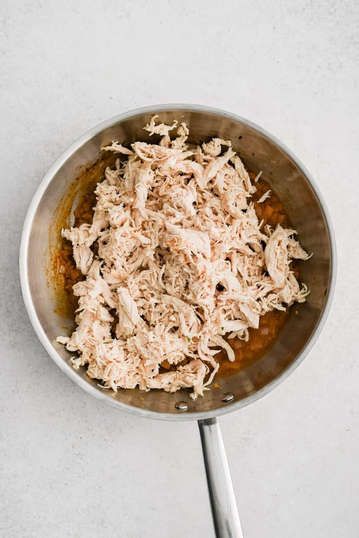 Shredded chicken added to a skillet filled with simmering chicken broth, onion, taco seasoning, and garlic.