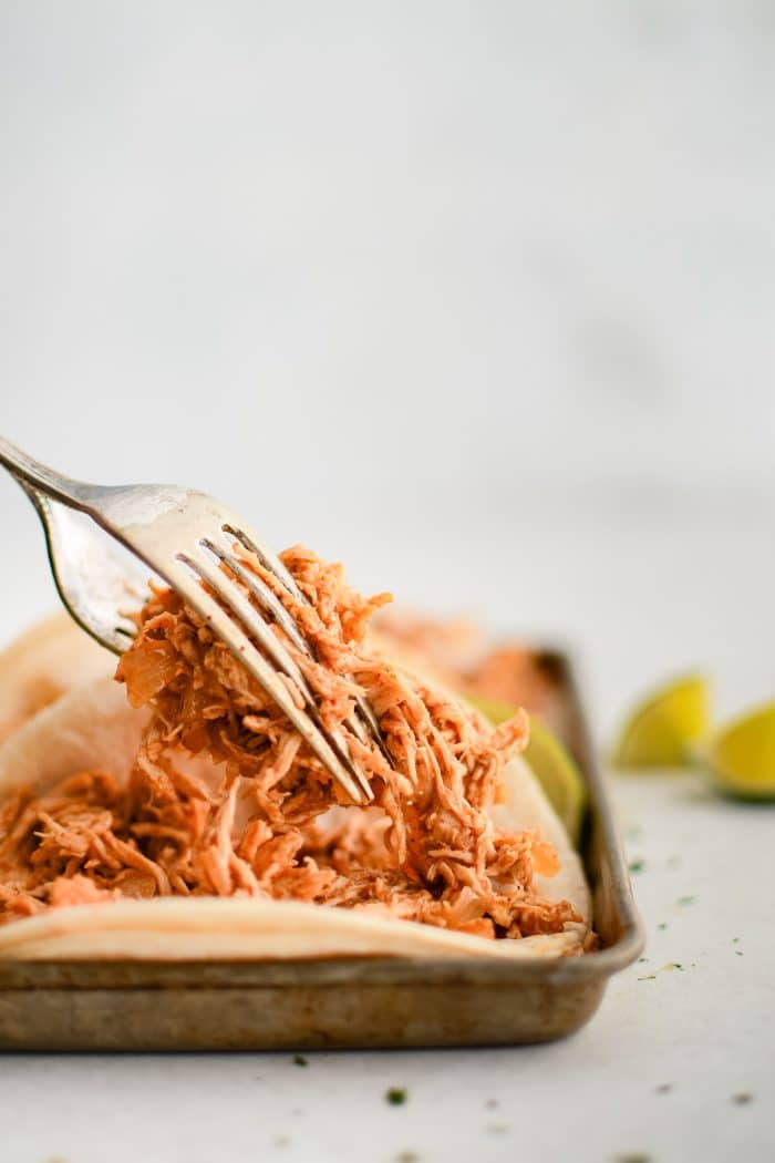 Two forks carefully topping corn tortillas with taco-seasoned shredded chicken.