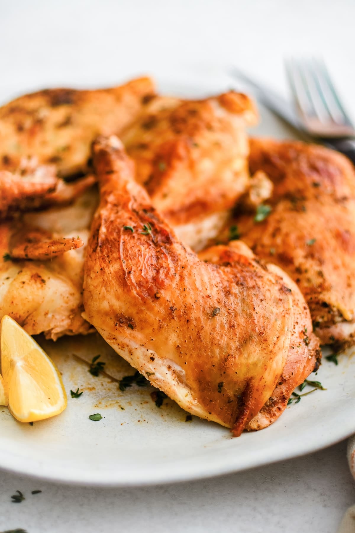 Juicy and golden roasted spatchcock chicken cut into pieces on a white serving plate and served with lemon wedges.
