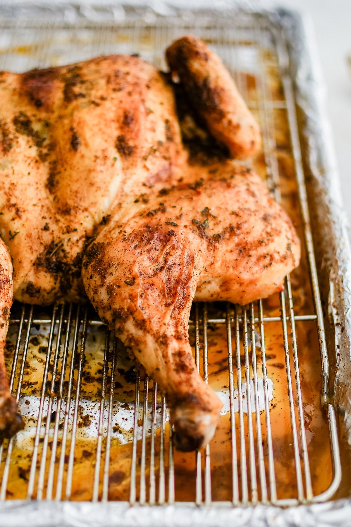 Juicy roasted spatchcock chicken resting on a metal cooking rack set inside a rimmed baking sheet.