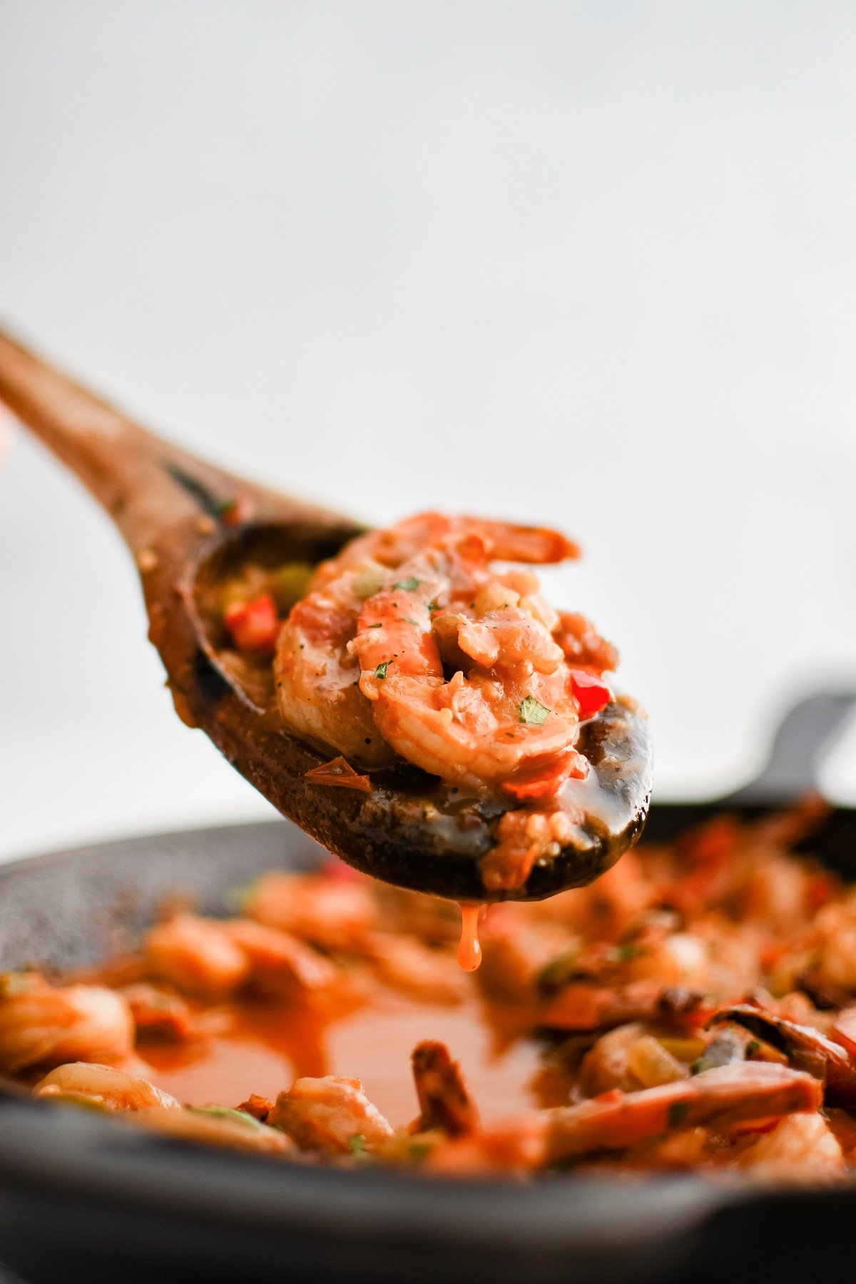 Wooden serving spoon filled with cooked shrimp in a spicy chipotle sauce with onions and bell peppers.
