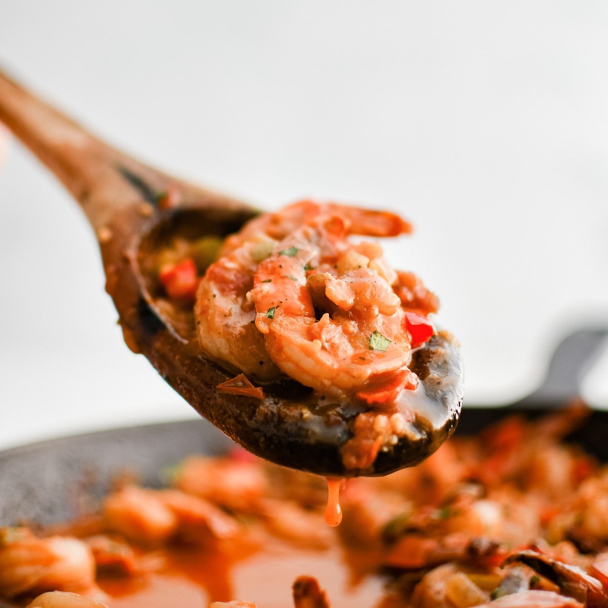 Wooden serving spoon filled with cooked shrimp in a spicy chipotle sauce with onions and bell peppers.