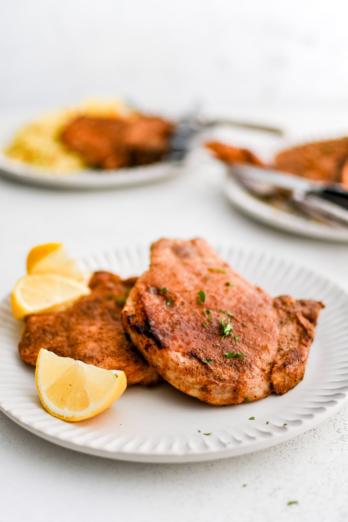 Two perfectly seasoned, golden bone-in pork chops on a white plate with lemon wedges.