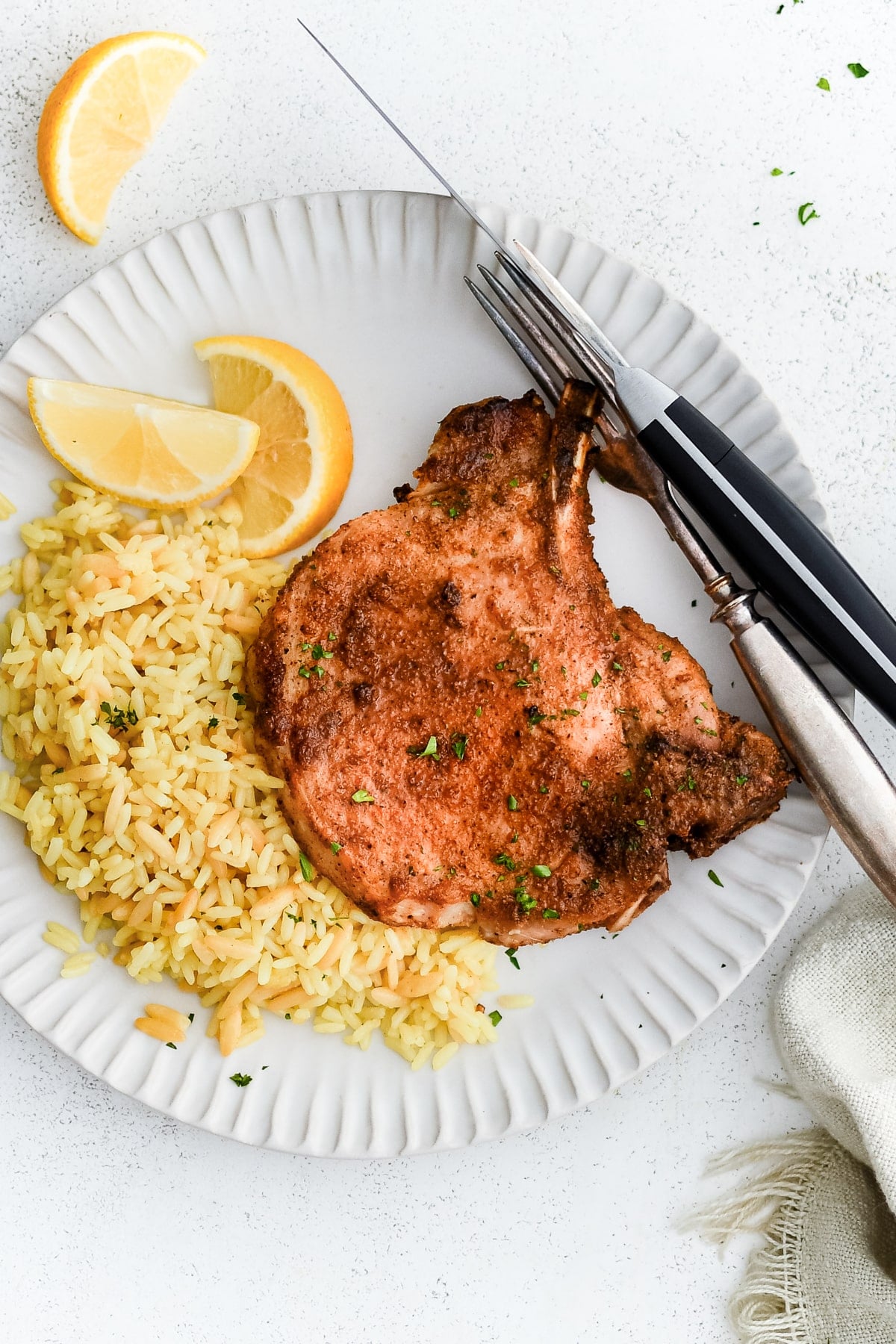 A perfectly seasoned, air-fried golden bone-in pork chop with yellow rice and lemon wedges on a white plate.