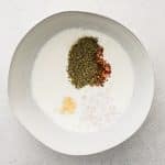 Bowl of buttermilk with garlic, shallots, Italian seasoning, red pepper flakes, and salt