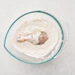 Chicken drumstick placed into seasoned flour dredge