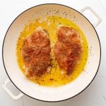 Two well-seasoned chicken breasts pan-frying in a large skillet.