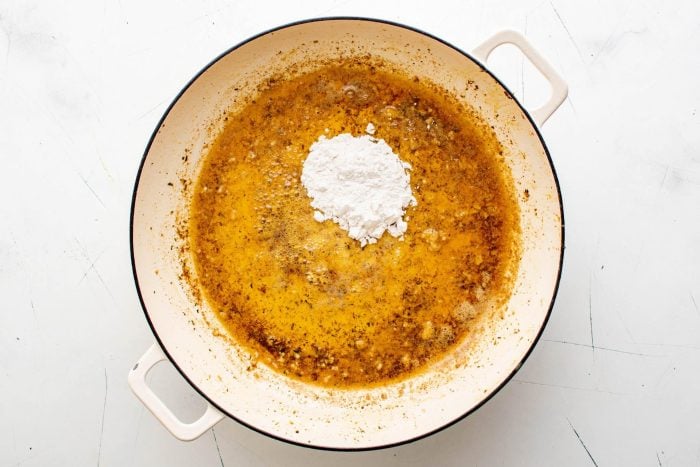 Flour is added to a large skillet filled with melted butter and fragrant minced garlic.