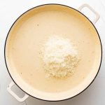 Adding freshly grated parmesan cheese to a large skillet filled with smooth and creamy sauce.