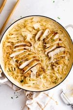 Large skillet with cooked fettuccine pasta coated in creamy Alfredo sauce, topped with two sliced chicken breasts and garnished with freshly grated parmesan cheese.