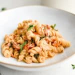Large shallow plate filled with cooked rotini pasta coated in a homemade creamy sun-dried tomato sauce.
