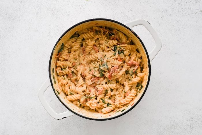 Large pot filled with cooked rotini pasta tossed in a cream-based sauce with sun-dried tomatoes, garlic, and spinach.