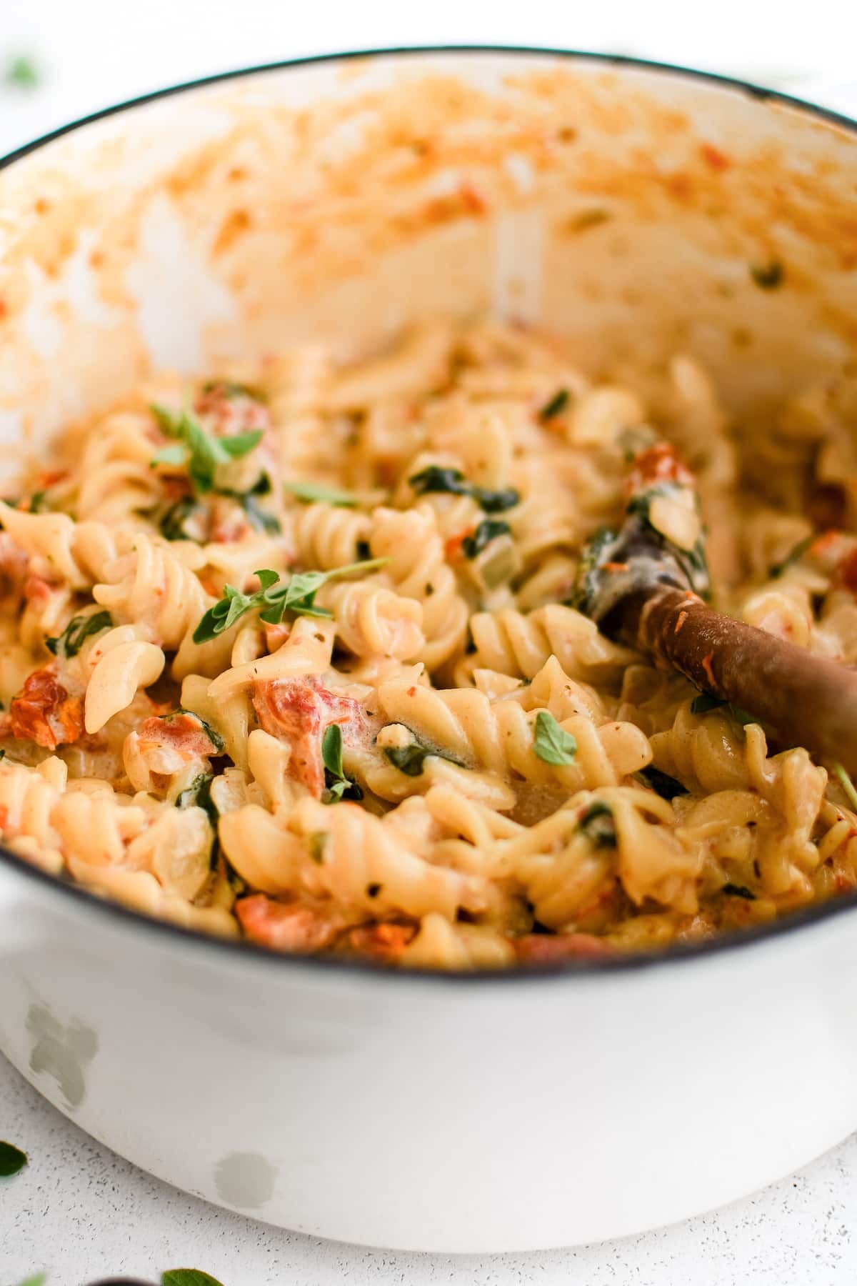 Large pot filled with cooked rotini pasta tossed in a cream-based sauce with sun-dried tomatoes, garlic, and spinach.
