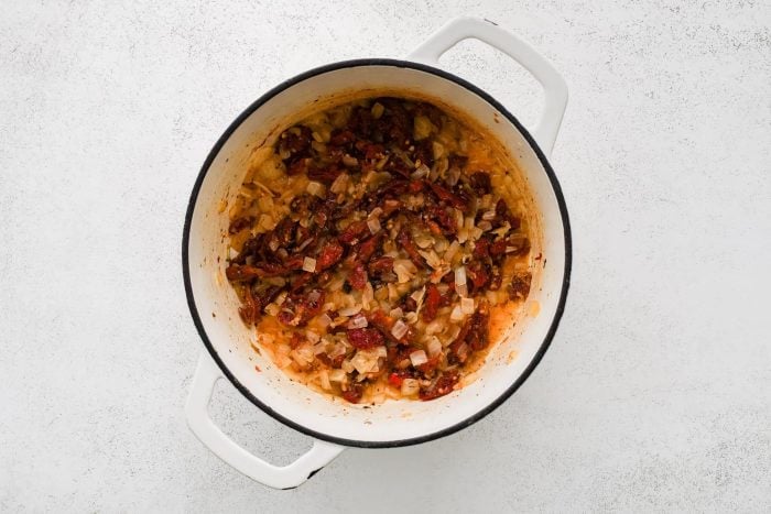 Softened onion, sun-dried tomatoes, garlic, salt, and dried oregano cooking in a large pot.