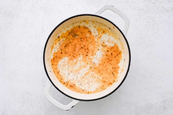 Heavy cream added to a large pot filled with softened onion, sun-dried tomatoes, garlic, salt, and dried oregano.