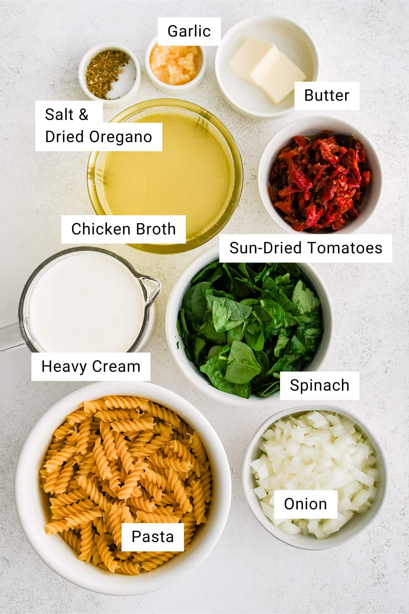 Ingredients for creamy sun-dried tomato pasta recipe are measured out and set aside in individual serving bowls.
