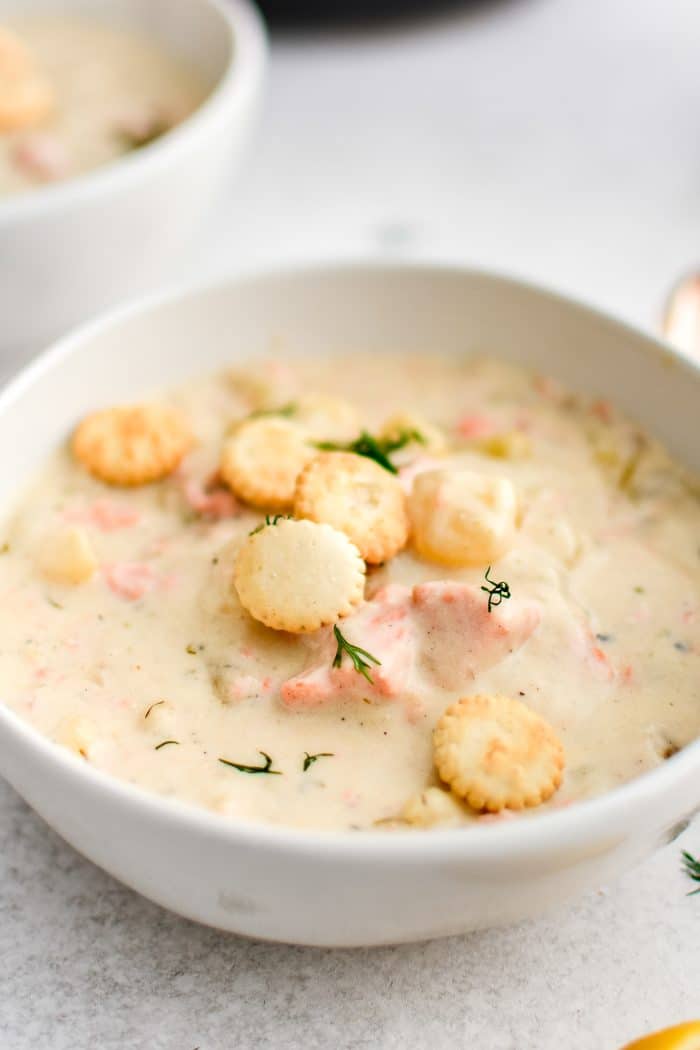 White bowl filled with thick and creamy salmon chowder with potatoes and fresh dill and garnished with Oyster crackers.