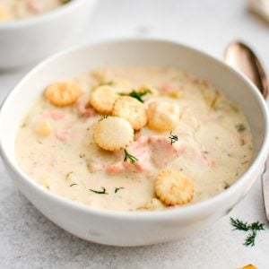 White bowl filled with thick and creamy salmon chowder with potatoes and fresh dill and garnished with Oyster crackers.