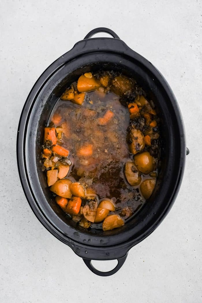 Cooked boneless pork butt removed from a large slow cooker filled with tender cooked potatoes, carrots, and onions in a savory garlic and herb broth.